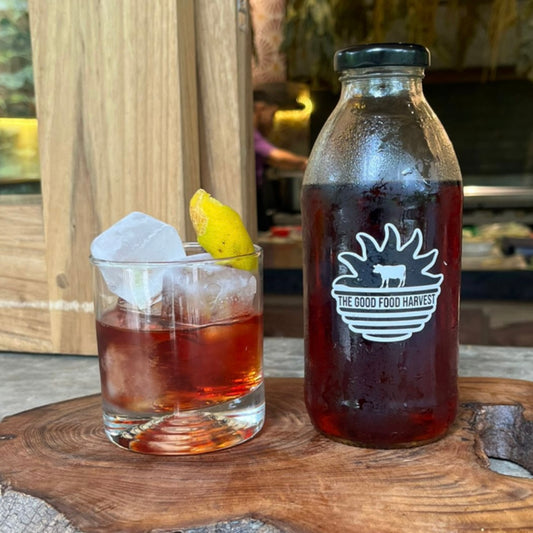 Bottle of 'The Good Food Harvest' juice and a glass with a drink on a wooden surface.